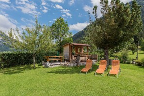 A wooden cabin with a deck, surrounded by a grassy area with lounge chairs and a picnic table.