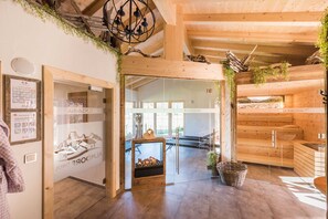 A wooden interior with a sauna area, a glass door entrance, and a view of the outdoors. - Chalet vacation home 11 - Almdorf Tirol (Haldensee)