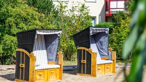Two wooden beach chairs with mosquito netting, positioned on sandy ground with dense greenery in the background.