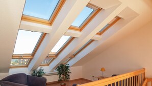 A spacious room with a sloped ceiling featuring skylights, a wooden staircase, a potted plant, and a chair.