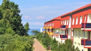 A row of colorful hotel buildings with balconies, a pathway, and a sailboat in the background.
