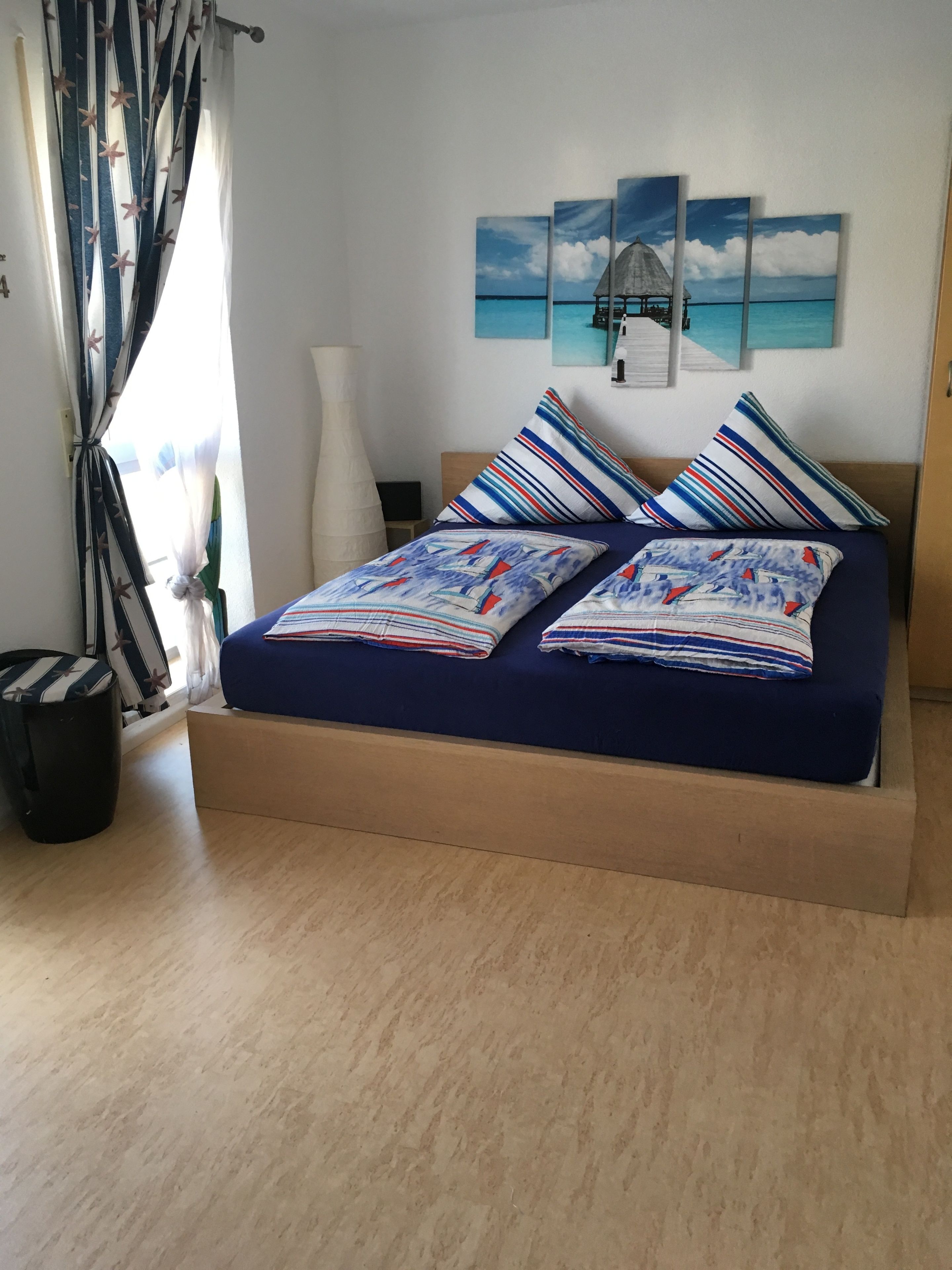 Ein Bett mit gestreifter Bettwäsche, ein Nachttisch, eine Lampe und eine Wand mit einem Gemälde.