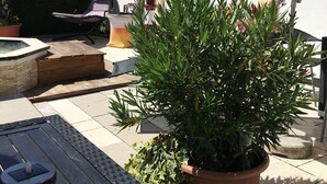 A patio with a yellow and white striped umbrella, a hot tub, and potted plants. - Gästehaus Tante Tienchen (Rust)