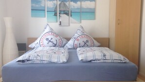 A bedroom with a bed, pillows, a nightstand, a vase, a wardrobe, and a wall with a seascape painting. - Gästehaus Tante Tienchen (Rust)