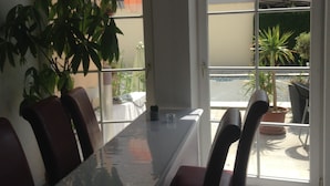 A dining area with a glass table and chairs, a potted plant, and a view of the outside through a glass door. - Gästehaus Tante Tienchen (Rust)