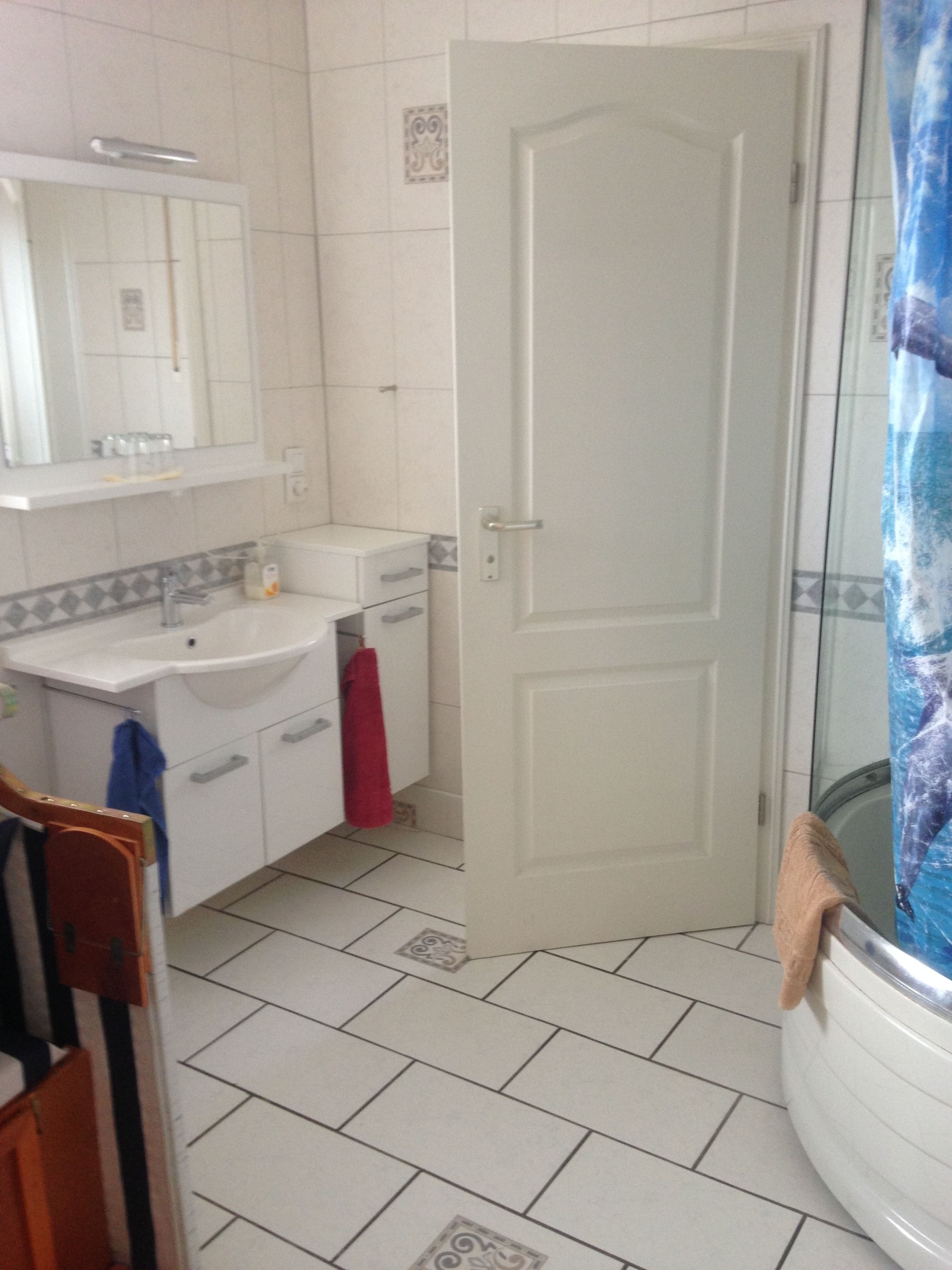 Ein Badezimmer mit einem weißen Waschbecken, Spiegel und Tür. Ein rotes Handtuch hängt am Türgriff.