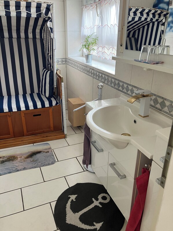 Ein Badezimmer mit gestreiftem Duschvorhang, einem Waschbecken mit Goldarmatur und einem gefliesten Boden.