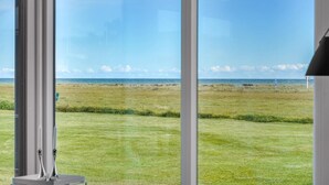 A view from a window overlooking a grassy beach area with a clear sky. - Cozy home in Sæby with house sea view (Sæby)