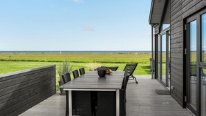 A deck with a table and chairs overlooking a grassy field and the ocean. - Cozy home in Sæby with house sea view (Sæby)