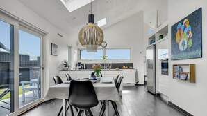 A modern kitchen with a dining area, large windows, and a unique pendant light. - Cozy home in Sæby with house sea view (Sæby)