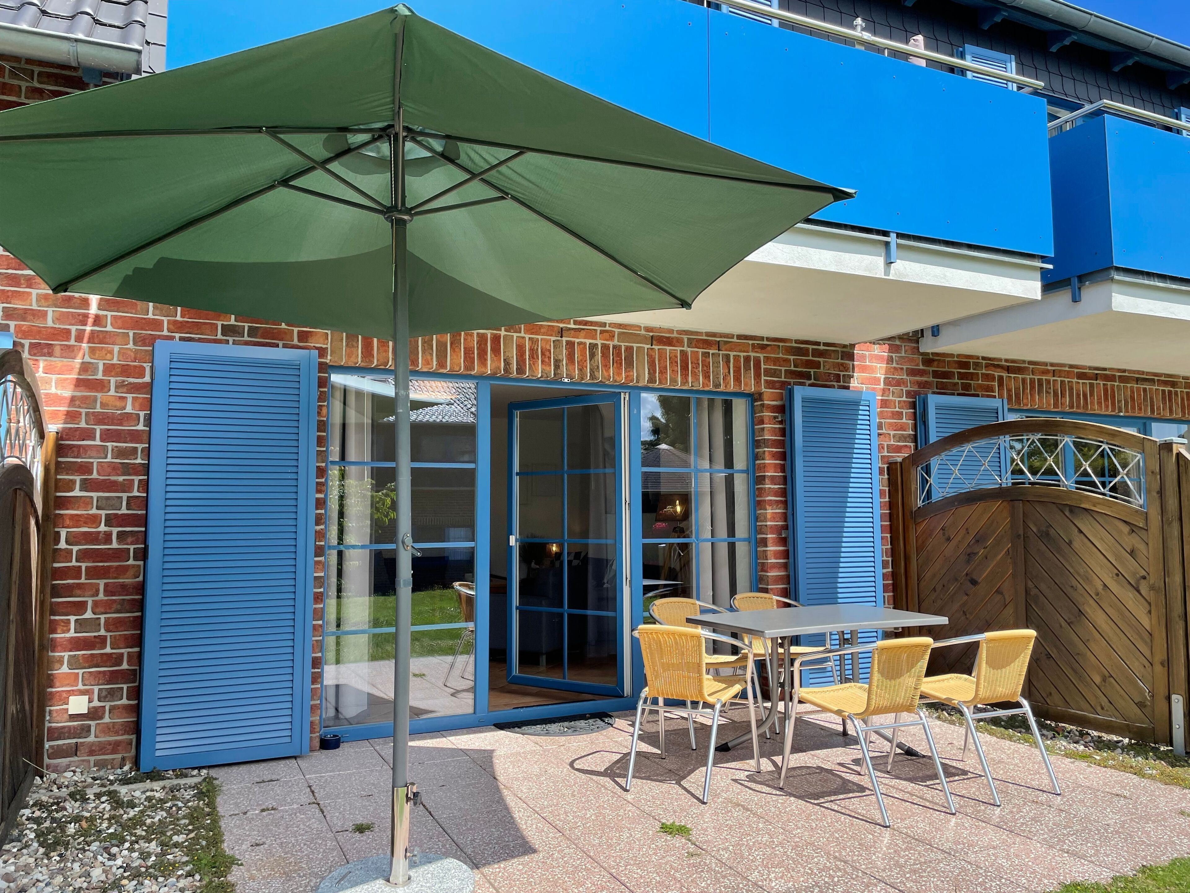 Eine Terrasse mit Tisch, Stühlen, einem grünen Sonnenschirm und einem Holzzaun.