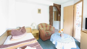 Una camera d'albergo con un letto, una sedia, un tavolino con un vaso di fiori, una lampada e una porta in legno.