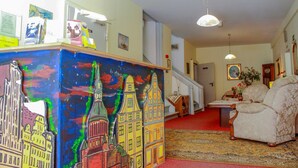 Una stanza con un'opera d'arte che raffigura un panorama urbano colorato, una moquette rossa, una poltrona bianca e una scala che conduce a un'altra stanza.
