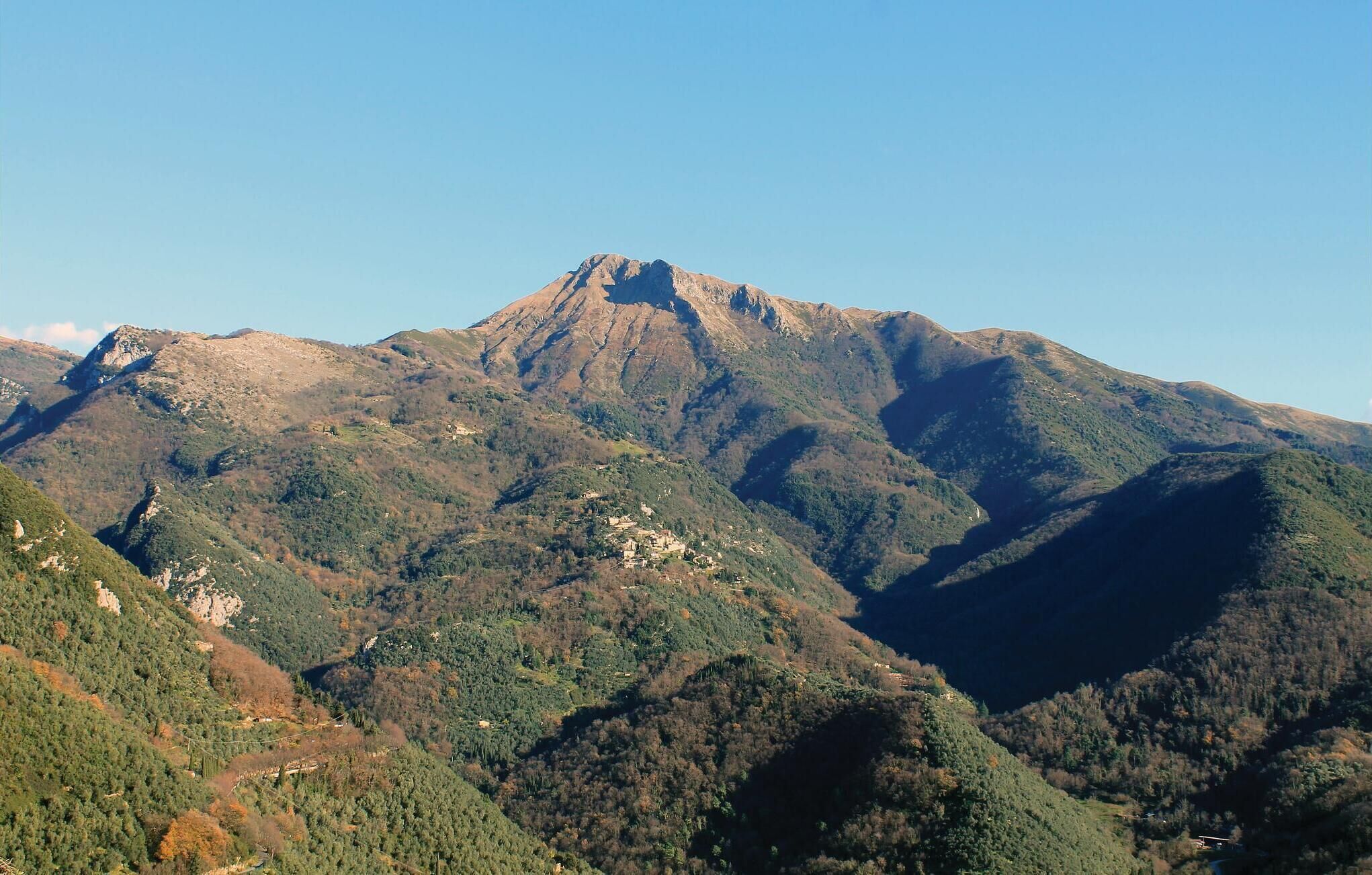 Un paisaje montañoso con un pico destacado, rodeado de zonas boscosas y edificios dispersos.
