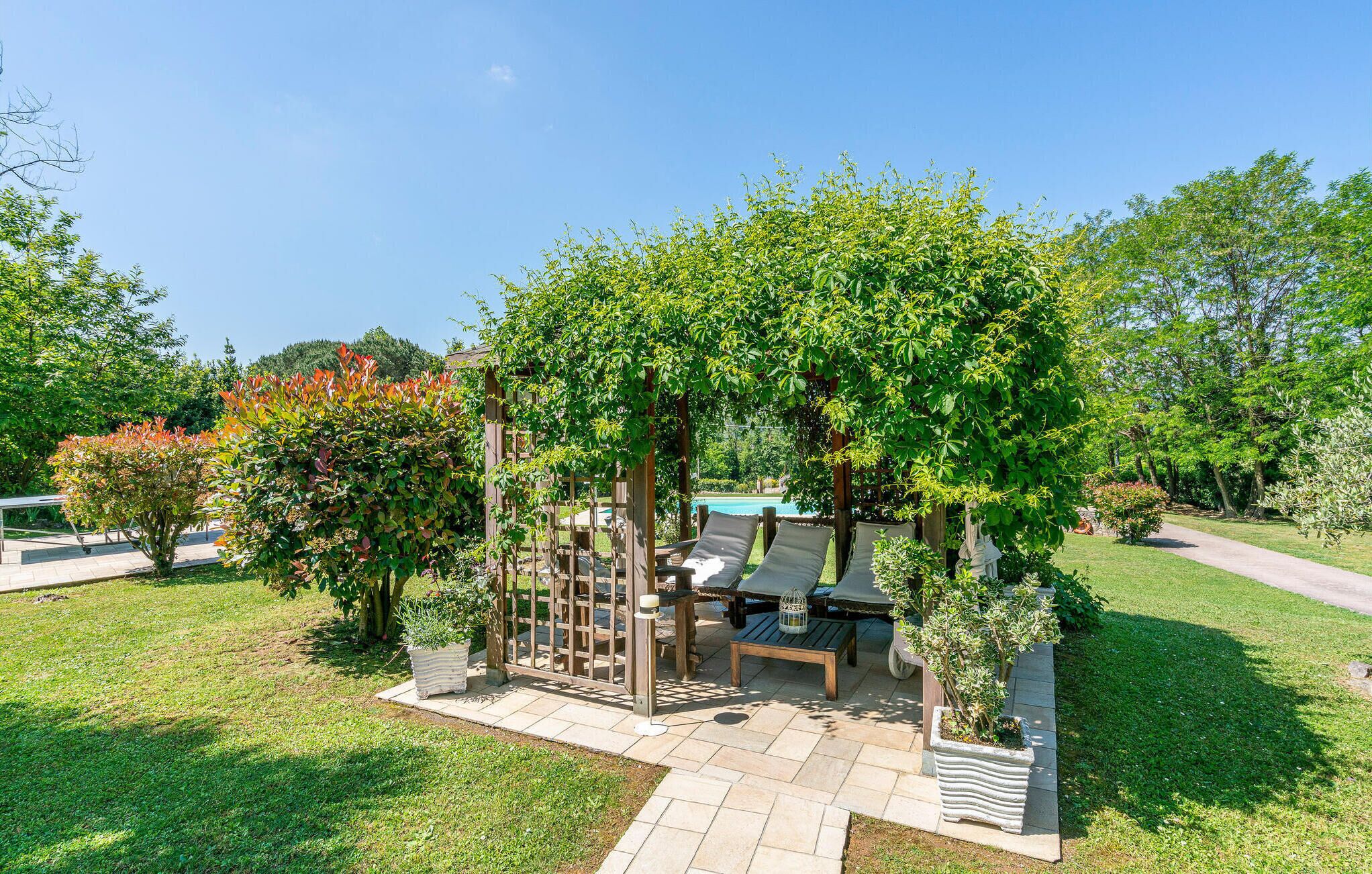 A garden with a pergola, seating area, and potted plants.