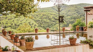 Une terrasse offrant une vue sur une colline verdoyante, des pots en terre cuite ornés de plantes et un panneau indicateur en métal.