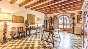 Une pièce avec un sol à carreaux, des poutres en bois au plafond, une table avec des chaises et une grande porte en arc donnant sur l’extérieur.