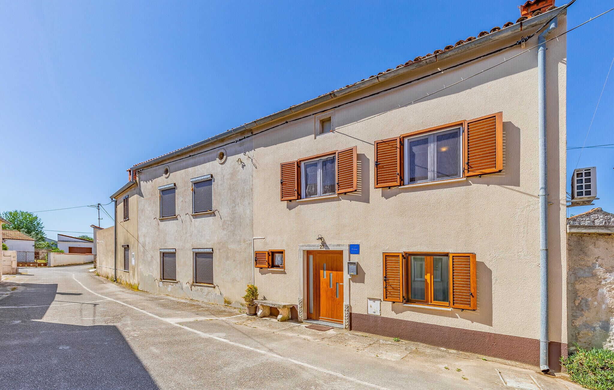 Un bâtiment à deux étages, doté d’une façade beige, de volets en bois aux fenêtres, d’un petit porche à l’avant et d’une porte bien visible.