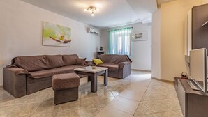 A living room with a brown sofa, a matching ottoman, and a small table. There is a window with curtains, a painting on the wall, and a ceiling light fixture. - Awesome home in Kavran with WiFi (Kavran)