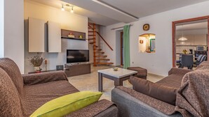 A modern living room with a flat-screen TV, a wooden staircase, and a dining area with a mirror and kitchen appliances. - Awesome home in Kavran with WiFi (Kavran)