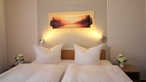 Een hotelkamer met een groot bed, twee nachtkastjes, een schilderij aan de muur, en een bloevas op elk nachtkastje.