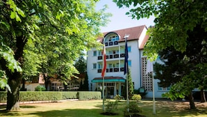 Een hotel met een centrale ingang, omgeven door verzorgde gazons en bomen.