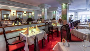 Een restaurant met meerdere tafels en stoelen, elk voorzien van een witte tafelkleed en een wijnglas.