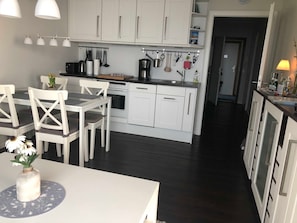 Cozinha moderna com armários brancos, uma mesa de jantar com cadeiras e um balcão com diversos eletrodomésticos e utensílios de cozinha.