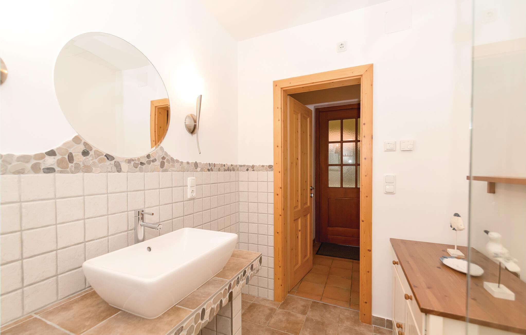 A bathroom with a large oval sink, a mirror, and a wooden door leading to another room.
