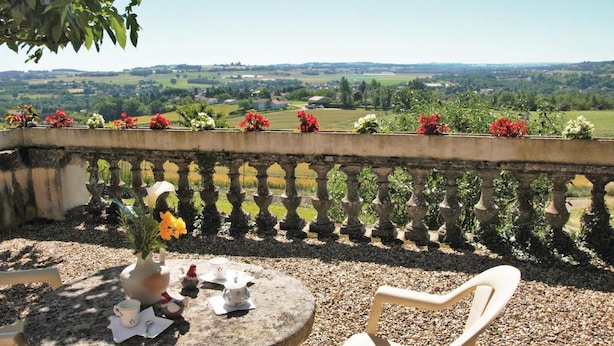 A balcony with a view of a green landscape, a table with a vase of flowers, and a chair. - Gorgeous home in Lavardac with kitchen (Lavardac)