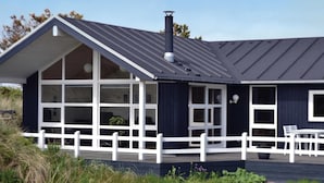 Et moderne hus med en stor veranda, hvide gelændere og et mørkt tag.