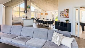 Een moderne woonkamer met een grijze bank, een eethoek met een ronde tafel en stoelen, en een keuken met witte kasten.