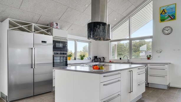 Een moderne keuken met een centraal eiland, roestvrijstalen apparatuur en grote ramen met uitzicht op groen.
