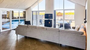 Een moderne woonkamer met een grote grijze bank, een flatscreen televisie en uitzicht op het buitenterras.