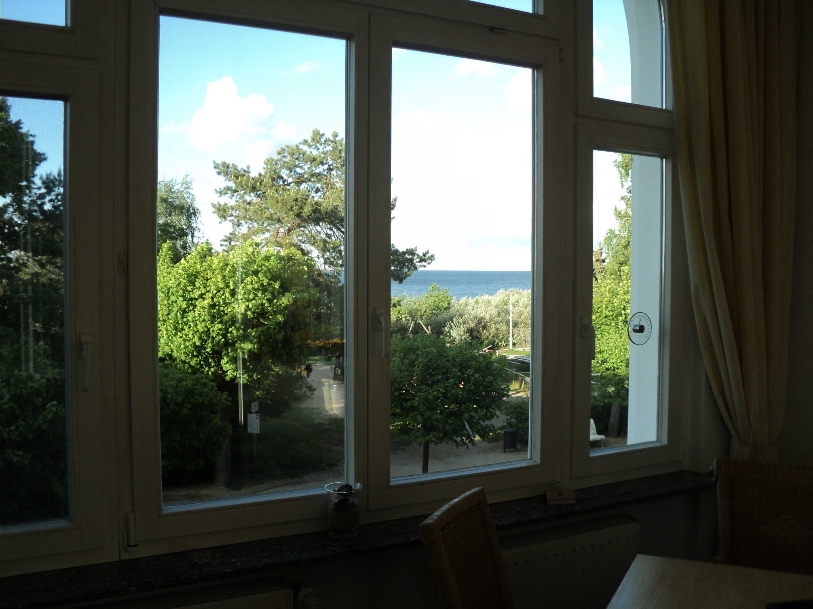 A room with large windows overlooking a garden and the sea.