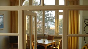 Un comedor con mesa y sillas, un televisor y vistas a árboles a través de amplias ventanas.