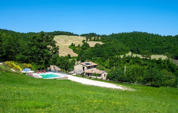 A rural setting with a swimming pool, stone buildings, and a hilly landscape.