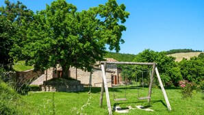 Ein Steinhaus mit einer Holzschaukel auf einer Rasenfläche.