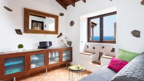 A bedroom with a bed, a wooden cabinet with glass doors, a small round table with a plant, and a window with a view of the sea. - La casita de la playa with jacuzzi (Santa Cruz de Tenerife)