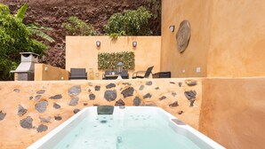 A hot tub with a stone wall backdrop, a small table with chairs, and a potted plant. - La casita de la playa with jacuzzi (Santa Cruz de Tenerife)