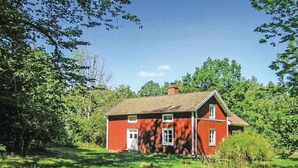 Ett rött trähus med ett sadeltak, omgivet av frodig grönska och träd.