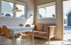 A room with a wooden interior, a white table with chairs, a sofa, and two windows with blinds. - Cozy home in Thyborøn with indoor swimming pool (Thyborøn)