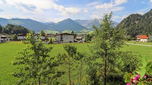 Un entorno rural con casas, un campo verde y montañas al fondo.