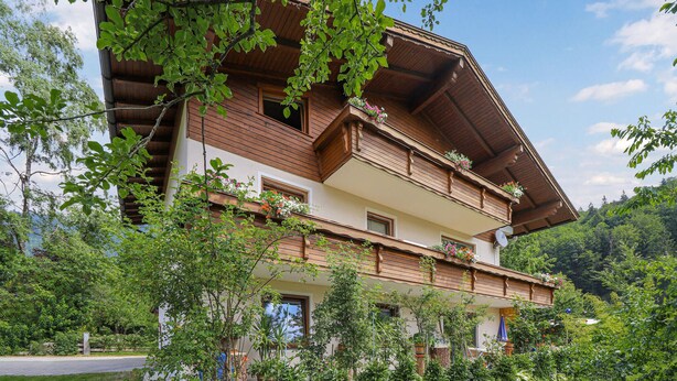 Una cabaña de madera tradicional con varios balcones, rodeada de vegetación exuberante y árboles.