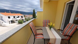 A balcony with a table and chairs, a view of buildings and mountains, and a yellow wall. - Holiday apartment with air conditioning (Šilo)