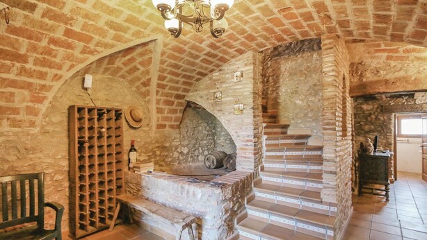 A rustic interior with a brick fireplace, a wine rack, and a staircase leading to an upper level. - Gorgeous home in Calonge (Calonge)