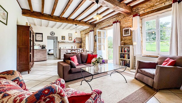 A spacious living area with a high ceiling, exposed wooden beams, a sofa set, a coffee table, a patterned rug, and a view of the outdoors through large windows. - Cozy home in St. Jean Aux Amognes (St. Jean Aux Amognes)