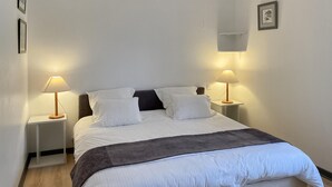 A neatly made bed with white bedding and a dark headboard, flanked by two bedside tables with lamps. - Cozy home in St. Jean Aux Amognes (St. Jean Aux Amognes)