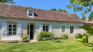 A two-story house with a tiled roof, a front door, and a small garden with a table and bench. - Cozy home in St. Jean Aux Amognes (St. Jean Aux Amognes)