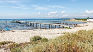 Una platja amb un moll de fusta que s'endinsa a la mar, una riba sorrenca i un edifici petit al fons.